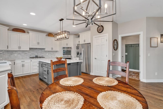 kitchen with white cabinets, appliances with stainless steel finishes, light countertops, an inviting chandelier, and dark wood finished floors