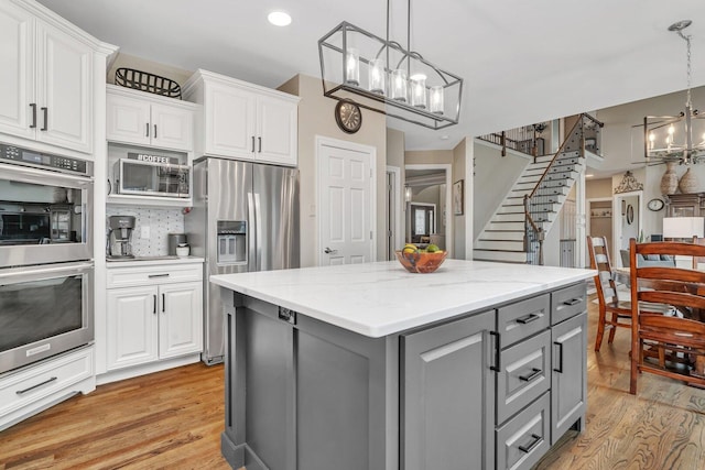 kitchen with white cabinetry, stainless steel appliances, an inviting chandelier, light wood-type flooring, and gray cabinets