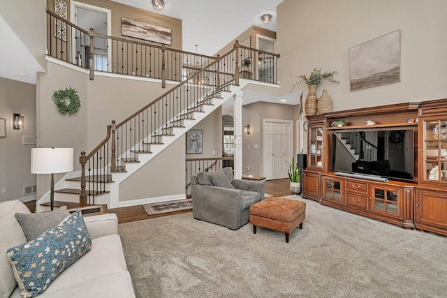 carpeted living area featuring baseboards, visible vents, stairs, and a high ceiling