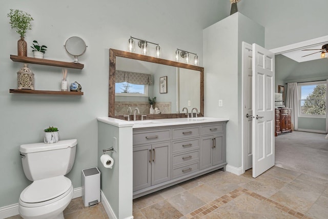 bathroom featuring a sink, ceiling fan, toilet, double vanity, and baseboards
