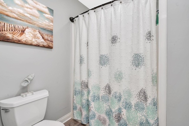 bathroom with toilet, a shower with curtain, wood finished floors, and baseboards