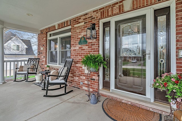 view of exterior entry featuring covered porch and brick siding