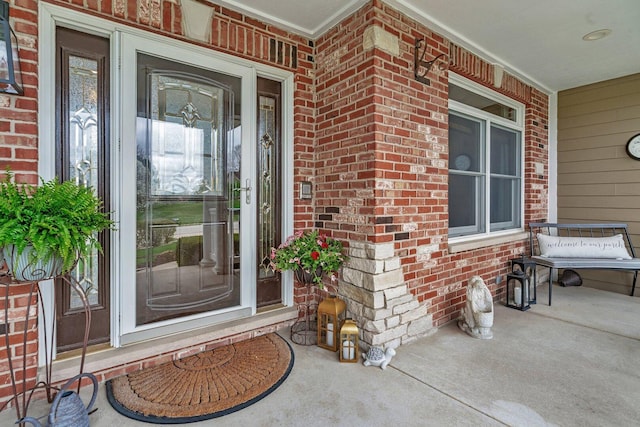 view of exterior entry with a porch and brick siding