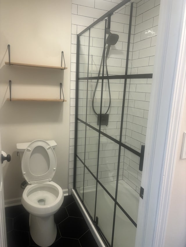 bathroom featuring toilet, a stall shower, tile patterned flooring, and baseboards