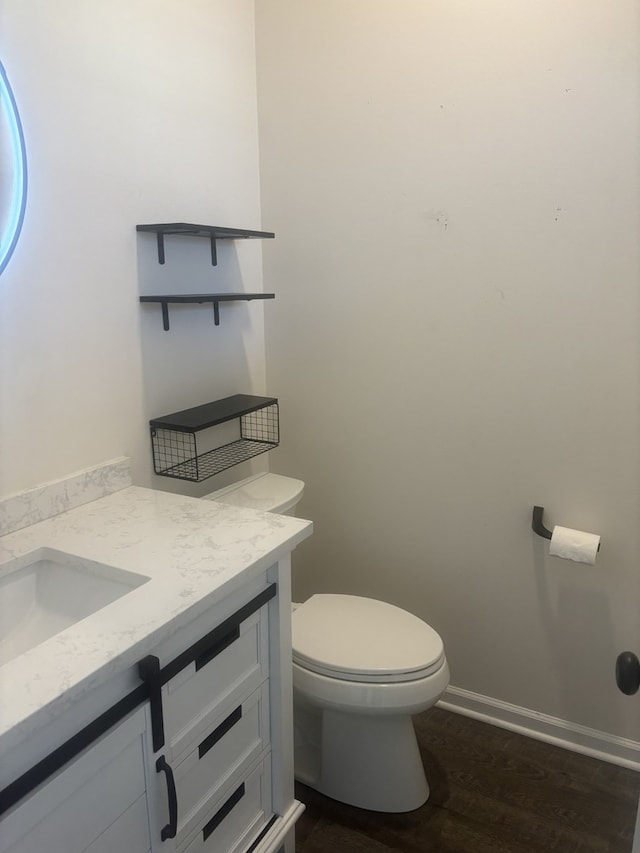 half bathroom featuring toilet, vanity, wood finished floors, and baseboards