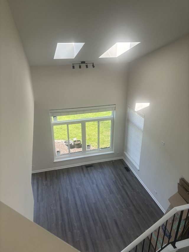 spare room with dark wood-style floors, a skylight, visible vents, and baseboards