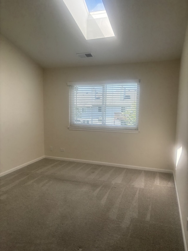 carpeted spare room with visible vents, baseboards, and a skylight