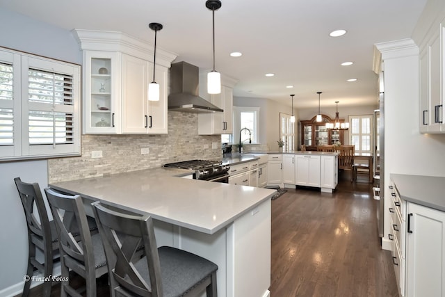 kitchen with wall chimney range hood, a peninsula, plenty of natural light, and gas range
