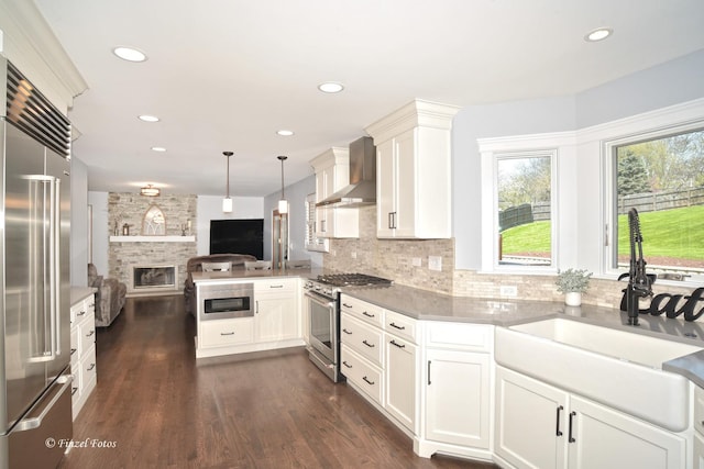 kitchen with a sink, premium appliances, backsplash, wall chimney range hood, and open floor plan