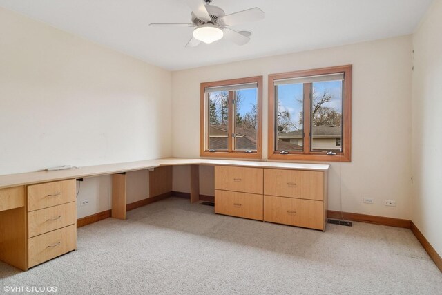 unfurnished office featuring light carpet, visible vents, baseboards, built in desk, and a ceiling fan