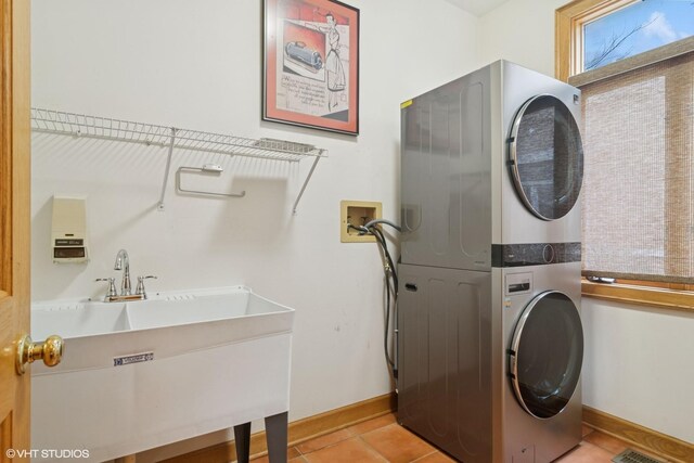 clothes washing area featuring laundry area, light tile patterned floors, a sink, stacked washing maching and dryer, and baseboards