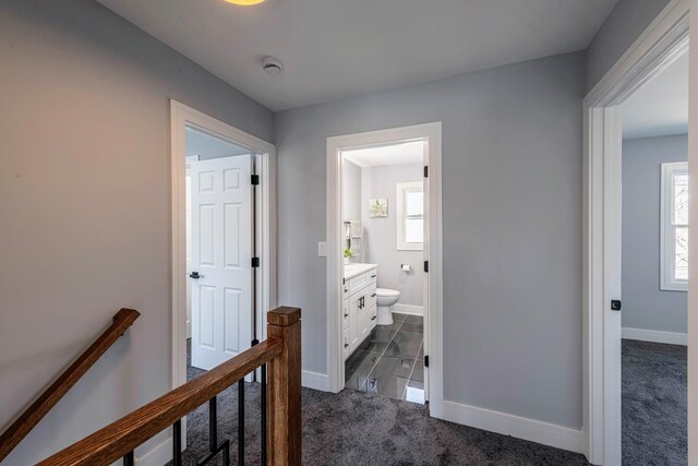 corridor with dark carpet, baseboards, and an upstairs landing