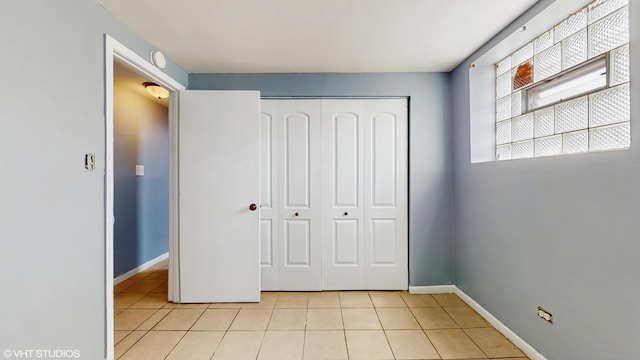 unfurnished bedroom with light tile patterned flooring, a closet, and baseboards