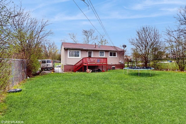 rear view of property with a deck, a trampoline, fence, and a lawn