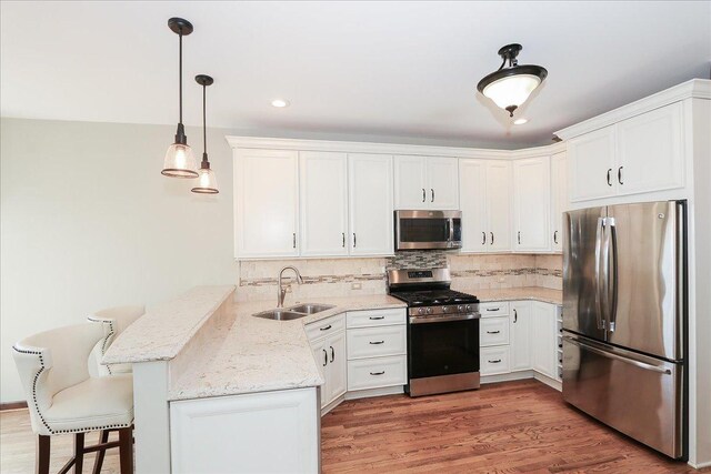 kitchen featuring decorative backsplash, appliances with stainless steel finishes, a sink, a peninsula, and white cabinetry