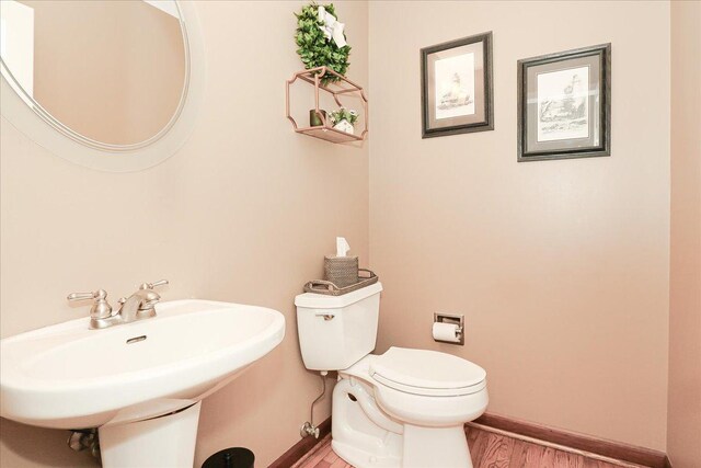 half bathroom with baseboards, a sink, wood finished floors, and toilet