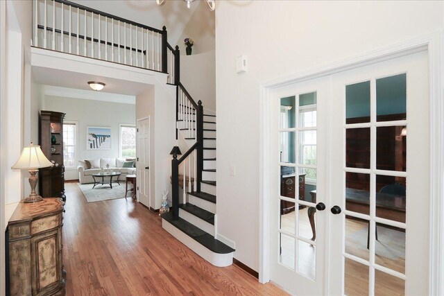 entryway with french doors, a towering ceiling, wood finished floors, baseboards, and stairs