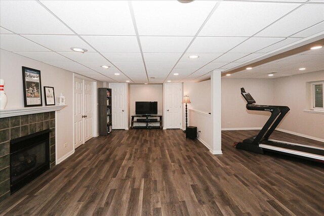 exercise area featuring wood finished floors, a tile fireplace, baseboards, a drop ceiling, and recessed lighting