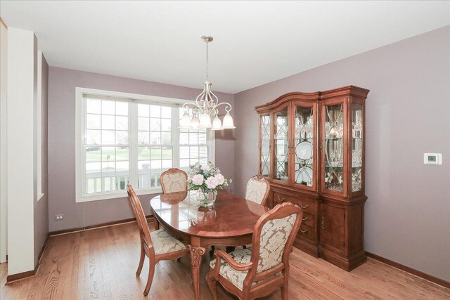 dining space with baseboards, a chandelier, and light wood finished floors