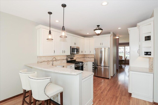 kitchen featuring a peninsula, white cabinetry, a sink, backsplash, and stainless steel appliances