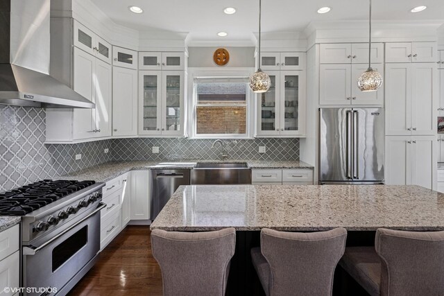 kitchen featuring white cabinets, a sink, high end appliances, pendant lighting, and wall chimney range hood