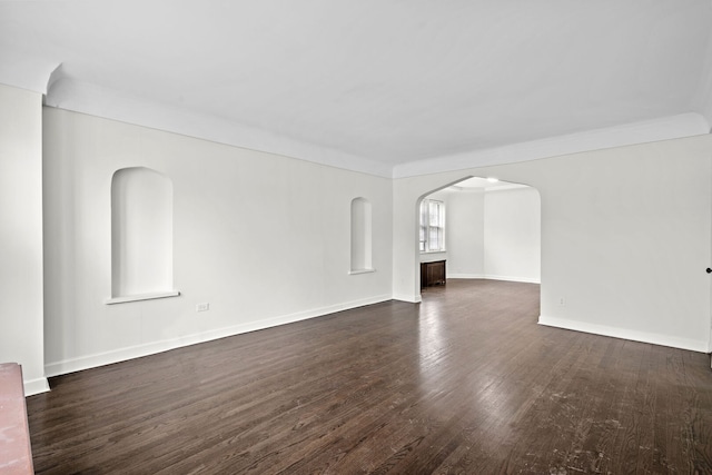 unfurnished living room featuring baseboards, wood finished floors, arched walkways, and ornamental molding