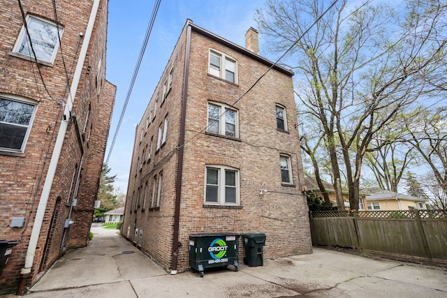 back of property featuring fence, a chimney, and brick siding