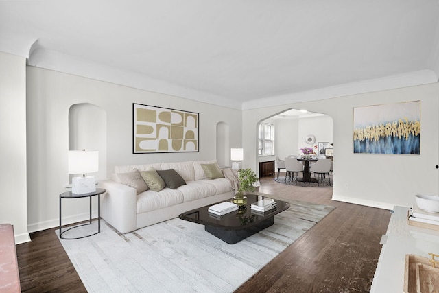 living area with arched walkways, wood finished floors, baseboards, and ornamental molding
