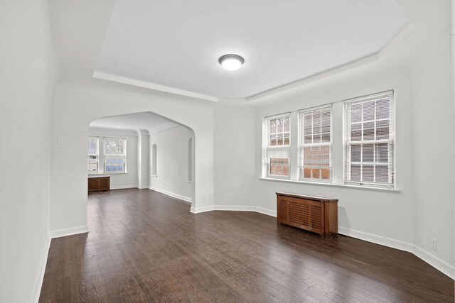 spare room with a raised ceiling, arched walkways, dark wood-style floors, and baseboards