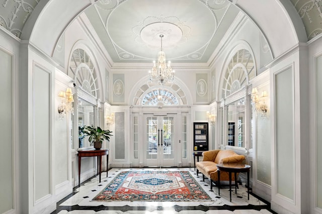 entrance foyer featuring crown molding, a decorative wall, a chandelier, french doors, and a towering ceiling