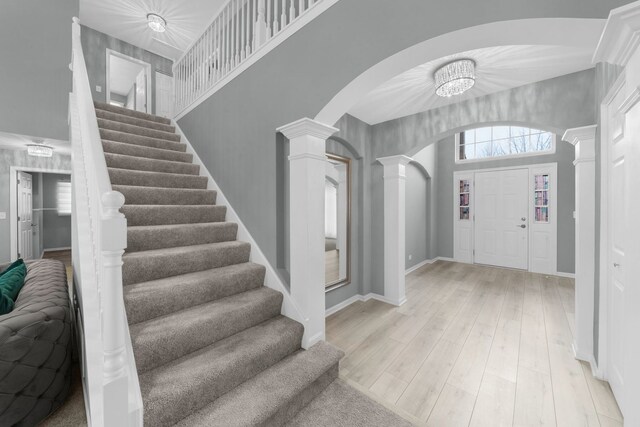 entryway with stairway, light wood-style floors, arched walkways, baseboards, and decorative columns