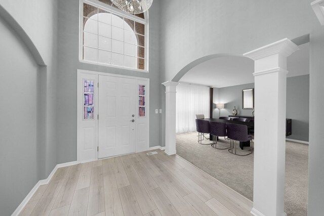 carpeted foyer featuring a towering ceiling, wood finished floors, arched walkways, baseboards, and decorative columns