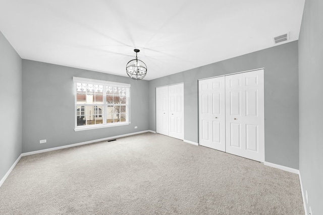 unfurnished bedroom featuring a chandelier, multiple closets, carpet flooring, and visible vents