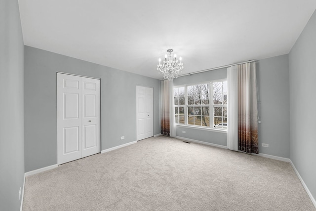 unfurnished bedroom featuring two closets, baseboards, a notable chandelier, and carpet flooring