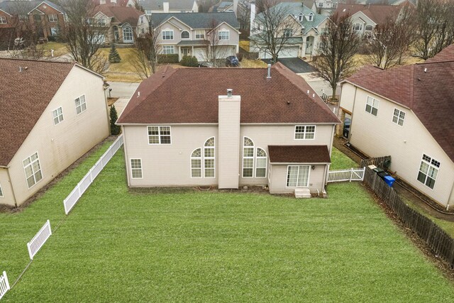 back of house featuring a chimney, a residential view, a fenced backyard, and a lawn