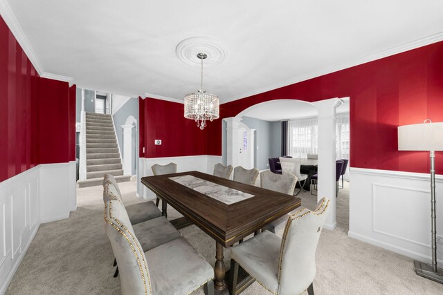 carpeted dining room featuring arched walkways, wainscoting, decorative columns, a chandelier, and stairs