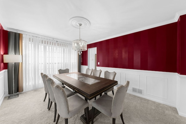 dining space featuring crown molding, wainscoting, an inviting chandelier, light colored carpet, and visible vents