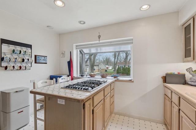 kitchen featuring baseboards, light floors, stainless steel gas stovetop, light brown cabinets, and tile counters