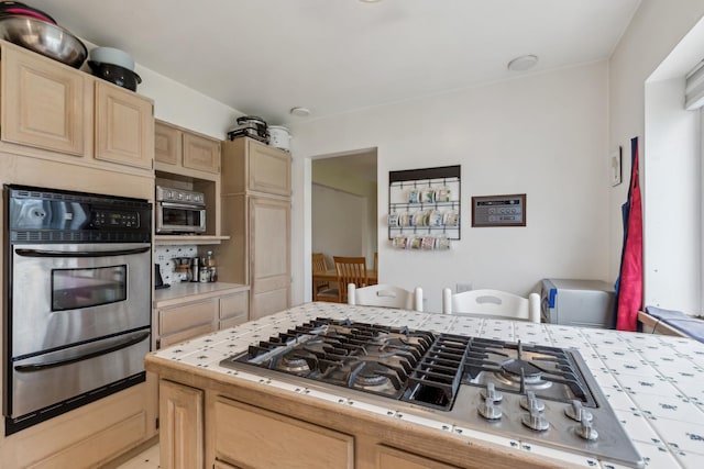 kitchen featuring tile countertops, light brown cabinetry, a warming drawer, and stainless steel appliances
