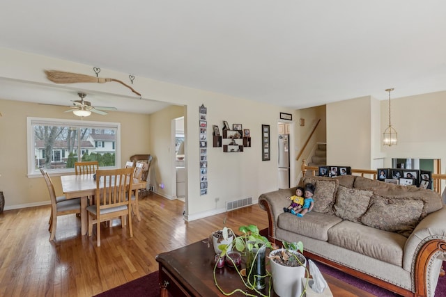 living room with visible vents, stairs, light wood-style floors, baseboards, and ceiling fan with notable chandelier