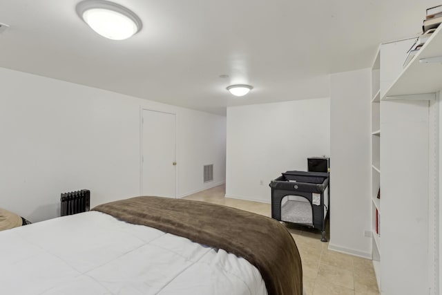 bedroom featuring light tile patterned floors, baseboards, visible vents, and radiator heating unit