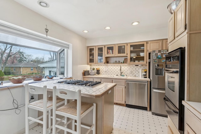 kitchen featuring a breakfast bar, stainless steel appliances, decorative backsplash, glass insert cabinets, and a warming drawer