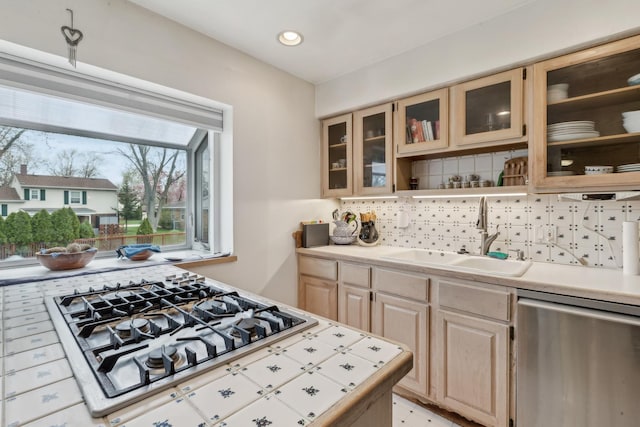 kitchen featuring decorative backsplash, light brown cabinetry, a sink, glass insert cabinets, and stainless steel appliances