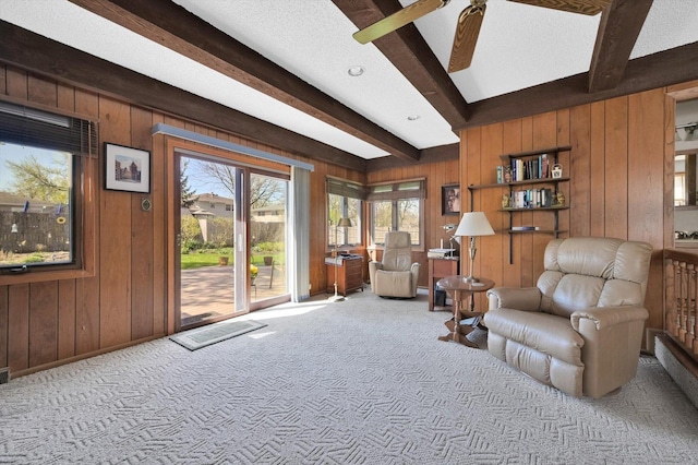 living area featuring beamed ceiling, a ceiling fan, wooden walls, and carpet
