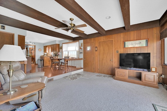 living room with beamed ceiling, wooden walls, a ceiling fan, visible vents, and light colored carpet