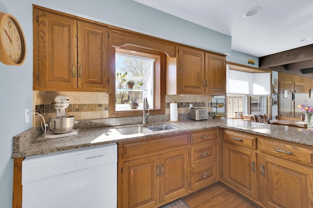 kitchen with brown cabinetry, a sink, backsplash, and white dishwasher