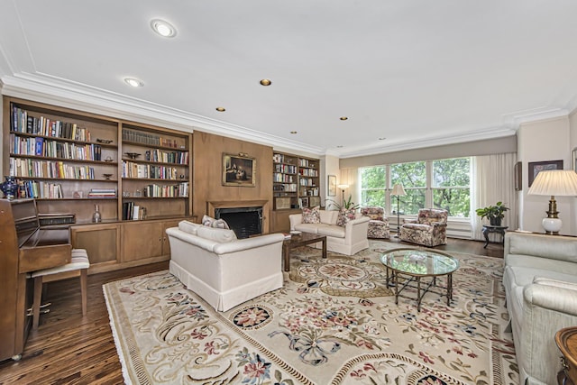 living area with built in shelves, ornamental molding, wood finished floors, and a fireplace