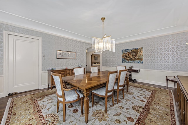 dining space with wallpapered walls, a wainscoted wall, wood finished floors, arched walkways, and a notable chandelier
