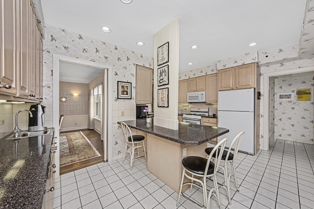 kitchen with wallpapered walls, a kitchen breakfast bar, a sink, and white appliances