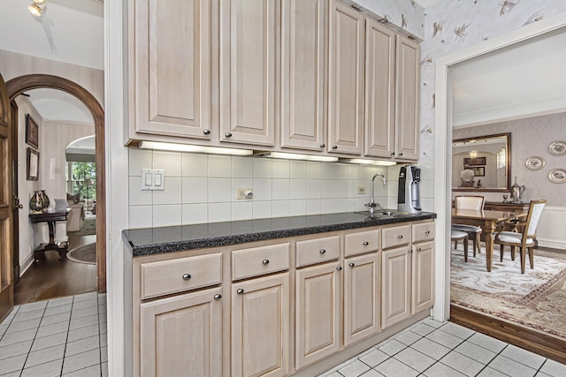 kitchen with arched walkways, wallpapered walls, light tile patterned floors, and a sink